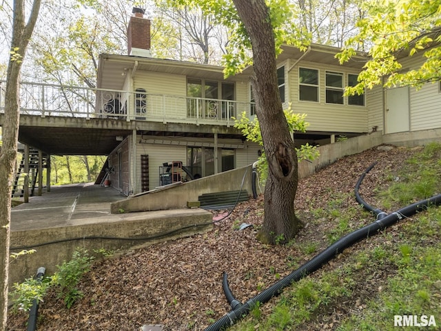 back of house featuring a wooden deck, a chimney, a patio area, driveway, and stairway