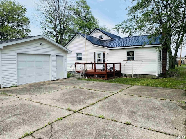 back of property featuring a garage, a deck, an outbuilding, driveway, and metal roof
