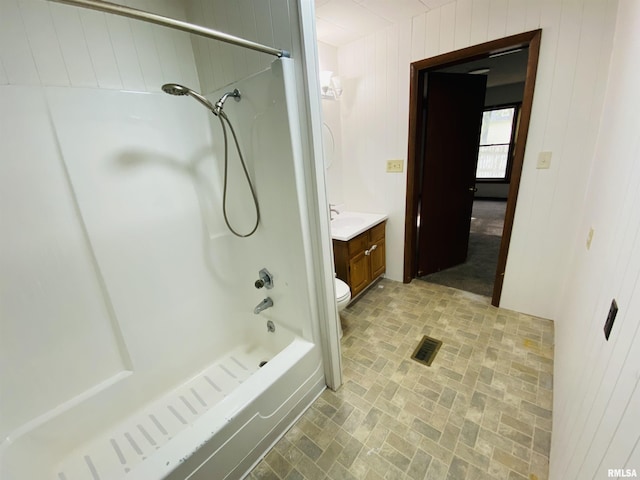 full bath featuring visible vents, vanity, brick patterned floor, wooden walls, and washtub / shower combination