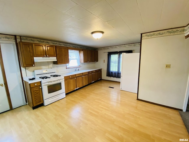 kitchen featuring light wood finished floors, white appliances, light countertops, brown cabinetry, and under cabinet range hood