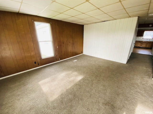 carpeted empty room with wood walls and a paneled ceiling