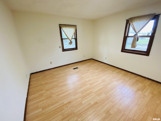 empty room featuring visible vents, light wood finished floors, baseboards, and a wealth of natural light