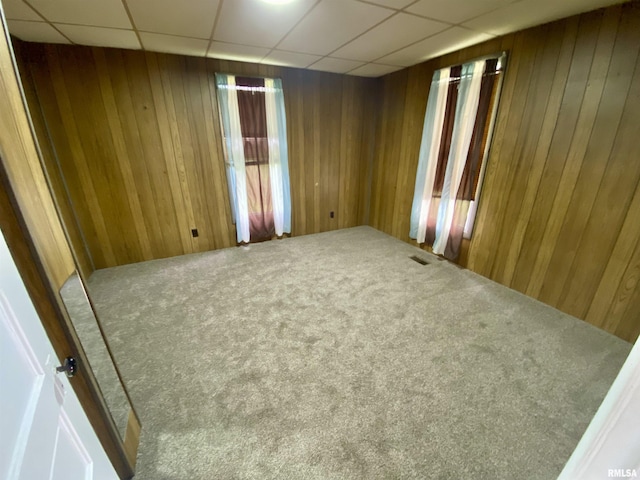 empty room featuring visible vents, carpet, wood walls, and a paneled ceiling