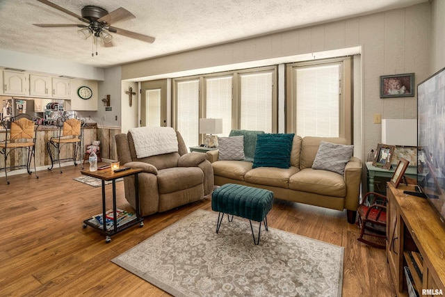 living area with a ceiling fan, a textured ceiling, and wood finished floors