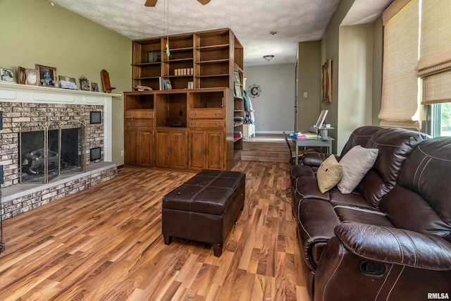living room with a textured ceiling, a ceiling fan, wood finished floors, and a brick fireplace