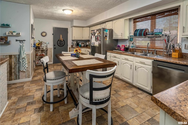 kitchen featuring a textured ceiling, appliances with stainless steel finishes, a sink, stone tile flooring, and white cabinetry