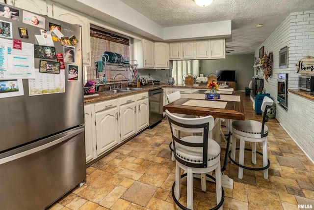 kitchen featuring dishwasher, a sink, white cabinets, freestanding refrigerator, and stone tile floors