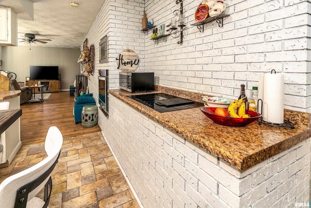 kitchen featuring black electric cooktop, ceiling fan, stainless steel oven, and brick wall