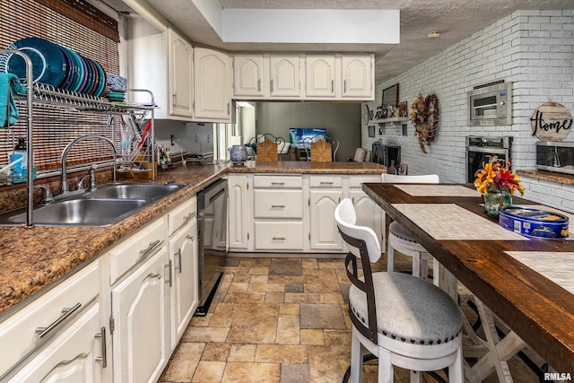 kitchen with stone tile flooring, a textured ceiling, white cabinets, a sink, and appliances with stainless steel finishes