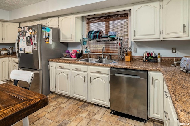 kitchen with white cabinets, dark countertops, appliances with stainless steel finishes, a sink, and stone finish floor