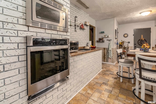 kitchen featuring stainless steel appliances, a textured ceiling, stone finish flooring, and brick wall