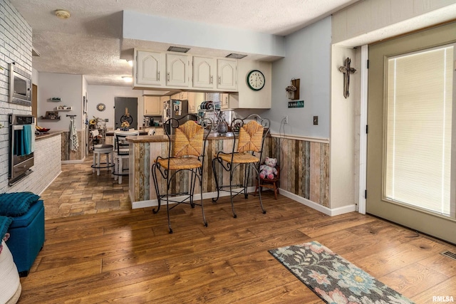 kitchen with a textured ceiling, a peninsula, wood finished floors, and stainless steel appliances