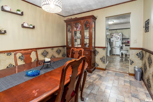 dining room featuring crown molding, stone tile floors, wainscoting, and a textured ceiling