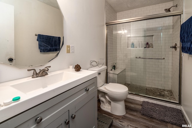 full bath with vanity, toilet, a textured ceiling, a shower stall, and wood finished floors