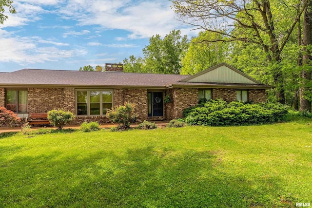 single story home featuring a shingled roof, a chimney, a front lawn, and brick siding
