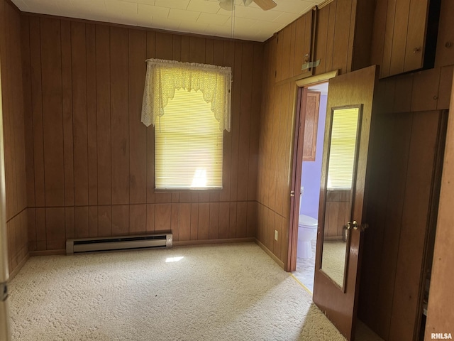 empty room featuring ceiling fan, light carpet, a baseboard heating unit, and wood walls