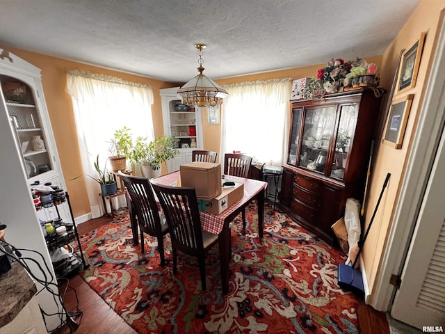 dining area with a textured ceiling, a notable chandelier, and dark wood-type flooring