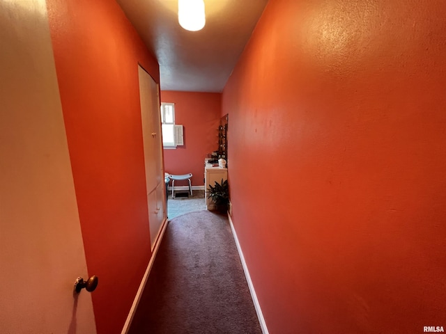 hallway featuring baseboards and dark carpet