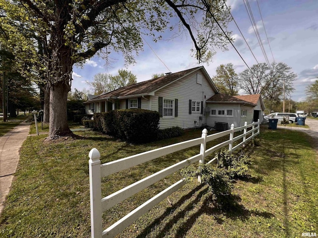 view of side of property featuring fence, a yard, and central AC