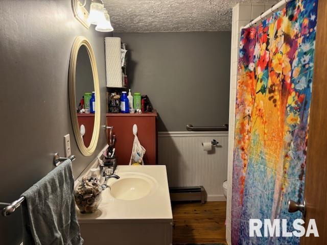 full bathroom with baseboard heating, vanity, a wainscoted wall, wood finished floors, and curtained shower