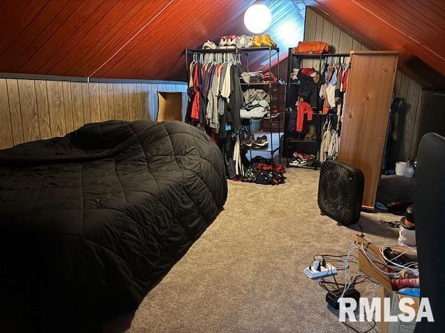 carpeted bedroom featuring wood walls and vaulted ceiling