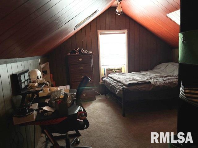 bedroom with wood walls, vaulted ceiling, and carpet flooring