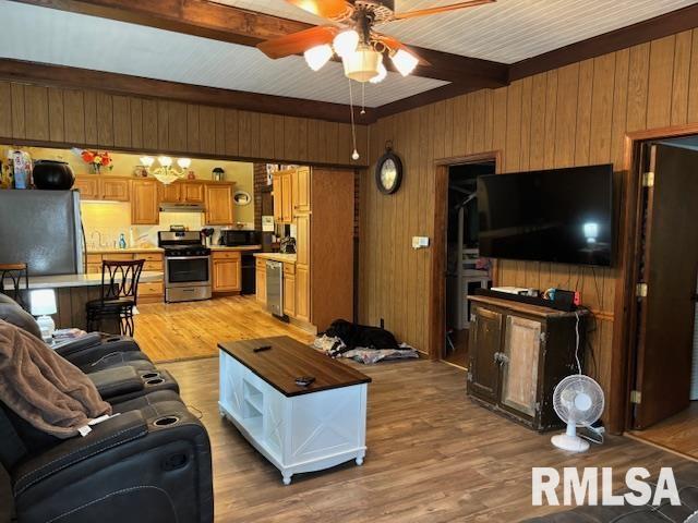 living room featuring light wood-style floors, wood walls, ceiling fan, and beamed ceiling