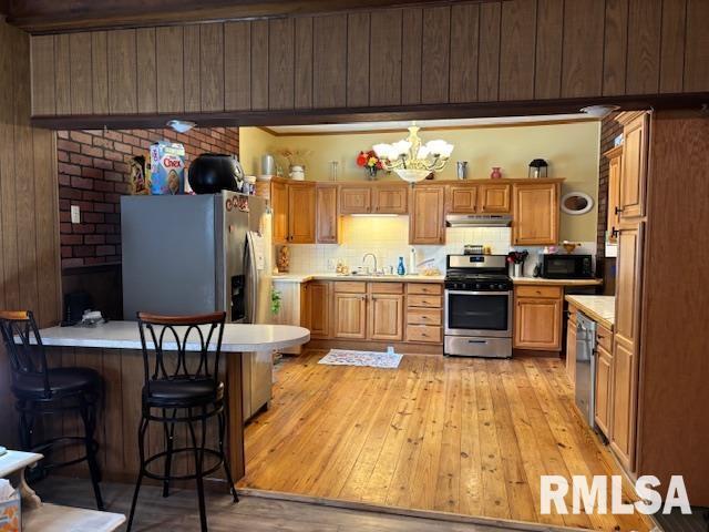 kitchen with a sink, light wood-style floors, light countertops, stainless steel appliances, and under cabinet range hood
