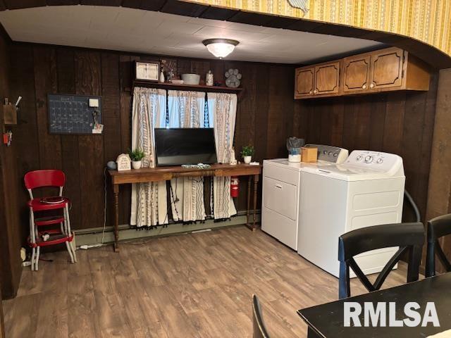 laundry room featuring separate washer and dryer, cabinet space, wooden walls, and light wood-style floors