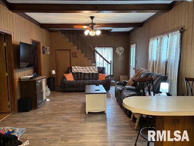 living room featuring wood finished floors, wooden walls, stairway, and beamed ceiling