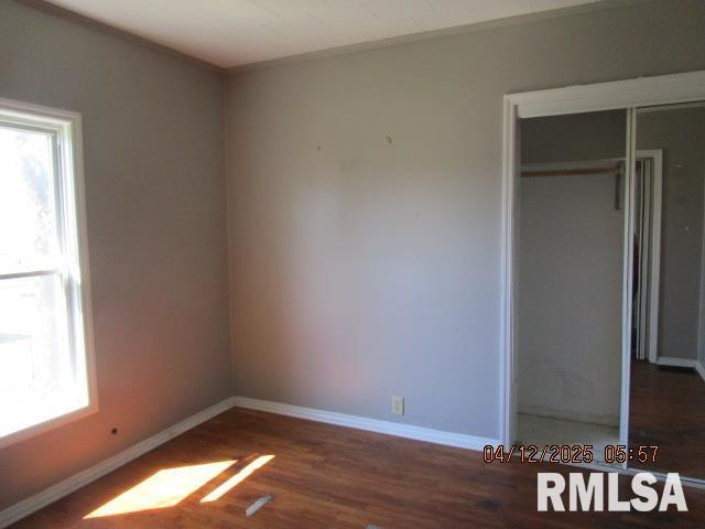 unfurnished bedroom featuring baseboards, multiple windows, wood finished floors, and a closet