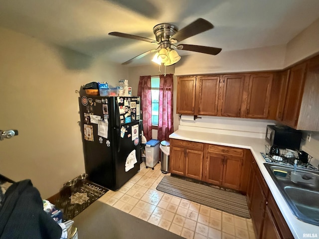 kitchen featuring a sink, light countertops, brown cabinetry, freestanding refrigerator, and a ceiling fan