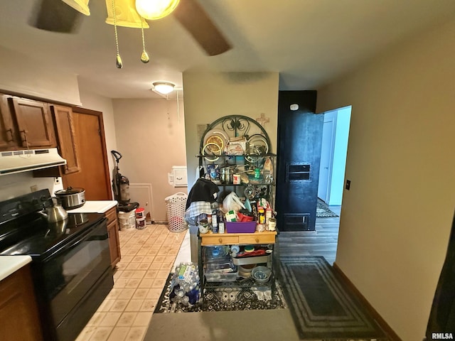 kitchen with black / electric stove, brown cabinetry, light tile patterned floors, light countertops, and under cabinet range hood