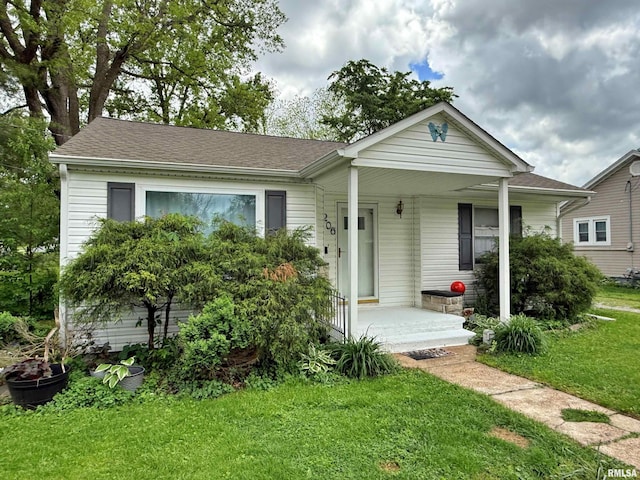 view of front facade with roof with shingles, covered porch, and a front yard