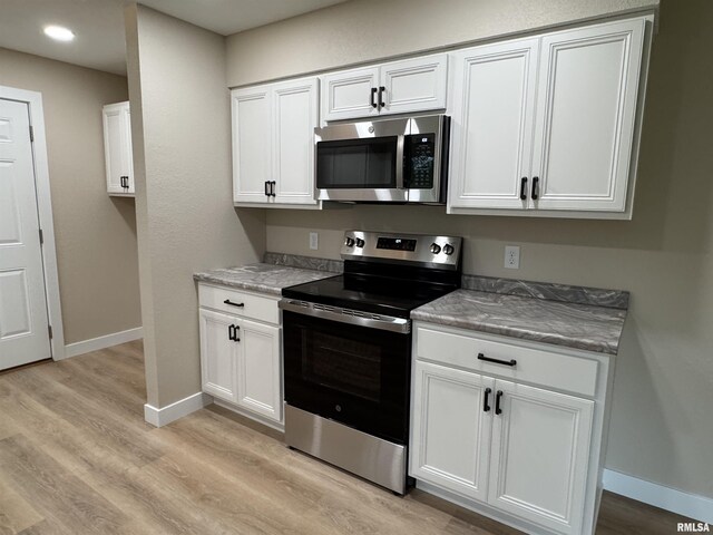 kitchen with stainless steel appliances, white cabinetry, and light wood-style flooring