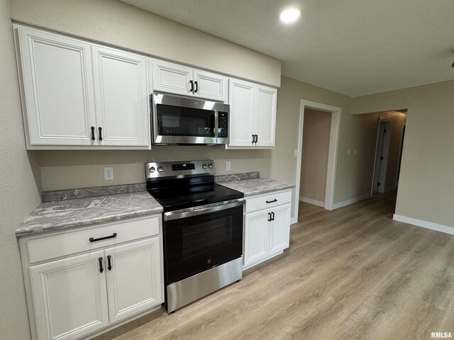 kitchen with white cabinets, light stone counters, stainless steel appliances, baseboards, and light wood-type flooring