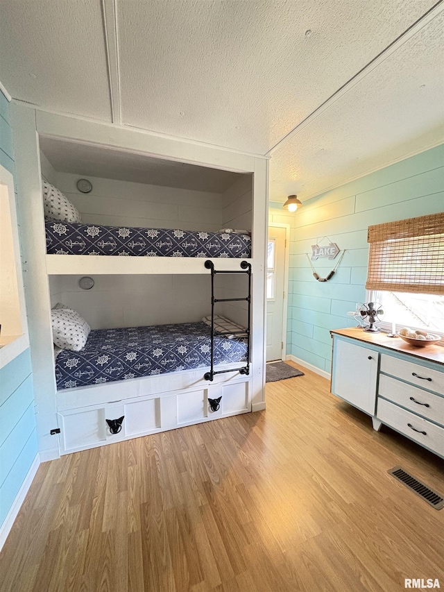 bathroom with a textured ceiling, visible vents, wood finished floors, vanity, and wooden walls