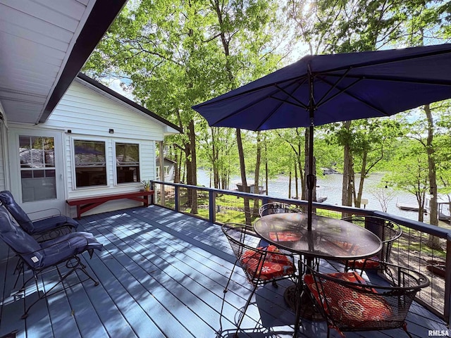 wooden terrace with a water view, an outbuilding, and outdoor dining space