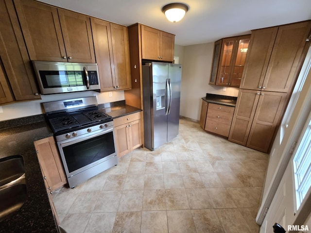 kitchen with glass insert cabinets, dark stone countertops, light tile patterned floors, and stainless steel appliances
