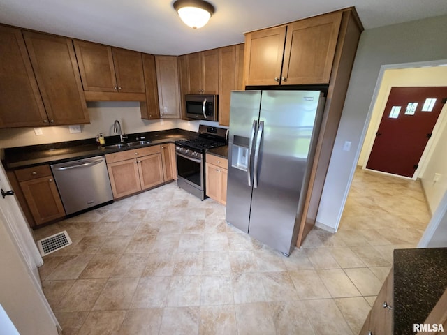 kitchen with visible vents, brown cabinetry, a sink, light tile patterned floors, and stainless steel appliances