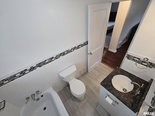full bath featuring visible vents, vanity, wainscoting, toilet, and tile walls