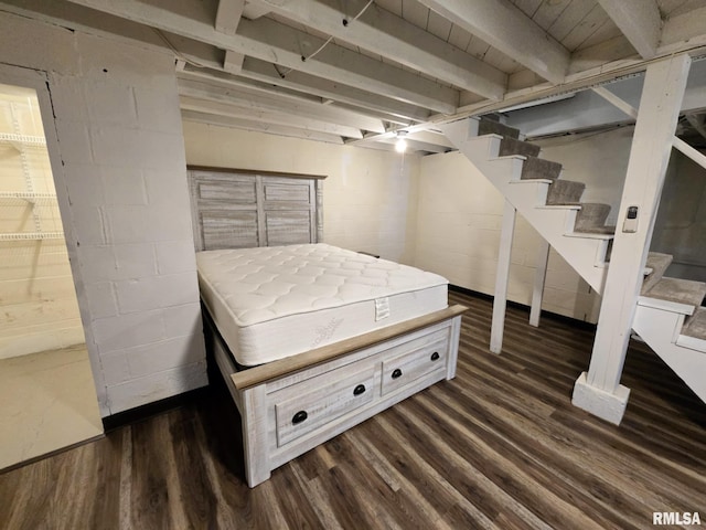 finished basement with concrete block wall, dark wood finished floors, and stairway
