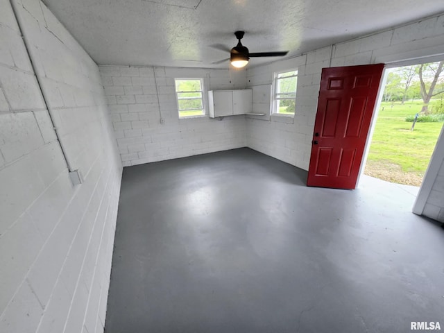 interior space with concrete block wall, ceiling fan, concrete floors, and a textured ceiling