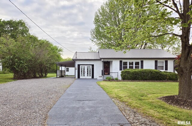 ranch-style home with a front yard, gravel driveway, stucco siding, french doors, and metal roof