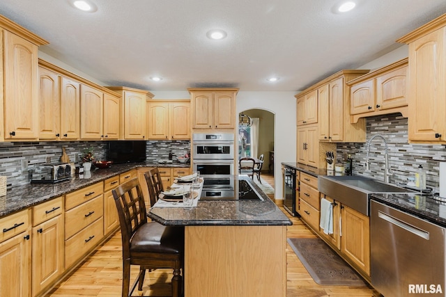 kitchen with light brown cabinetry, appliances with stainless steel finishes, arched walkways, and beverage cooler