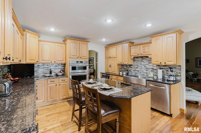 kitchen featuring light wood-style floors, a sink, appliances with stainless steel finishes, and light brown cabinets