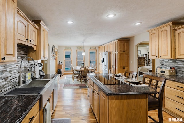 kitchen featuring decorative backsplash, high quality fridge, a textured ceiling, arched walkways, and light wood finished floors