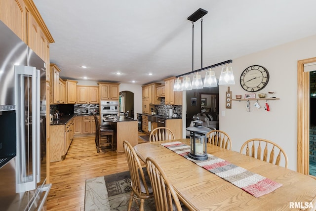 dining space with recessed lighting, arched walkways, and light wood finished floors