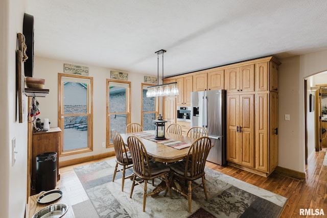 dining area featuring arched walkways, baseboards, and light wood-style flooring