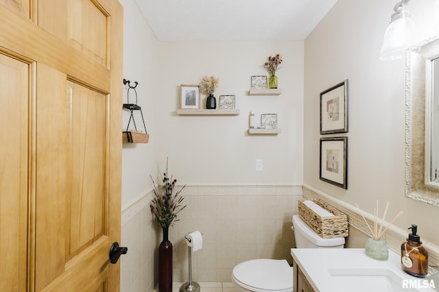 bathroom featuring toilet, tile walls, wainscoting, and vanity